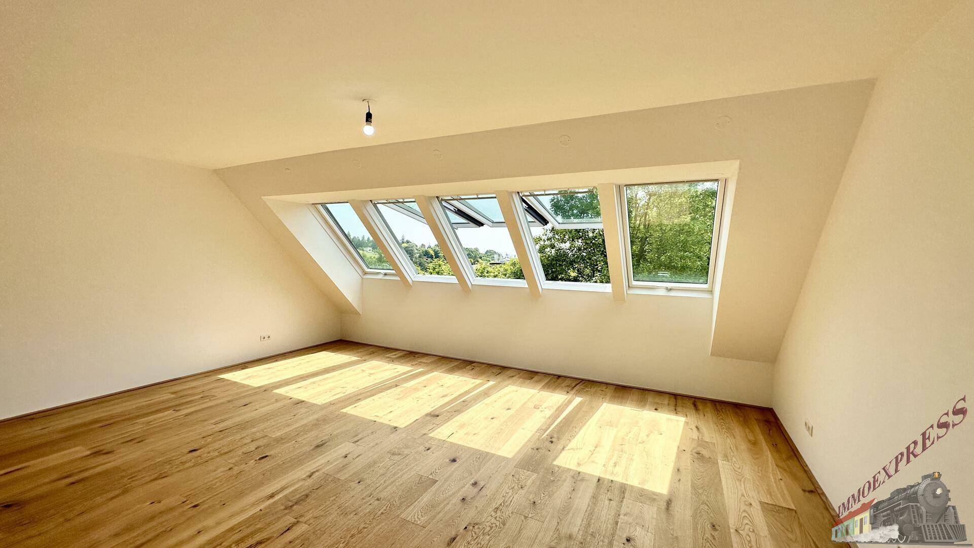 Helles Dachgeschosszimmer mit Holzboden und geöffneten Dachfenstern, die frische Luft hereinlassen.