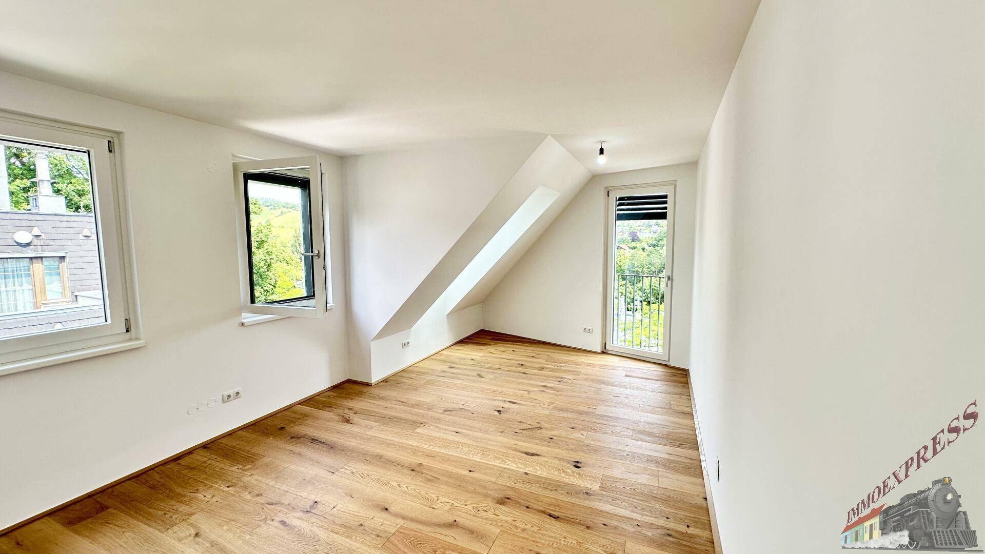 Helles Schlafzimmer mit Holzboden, großen Fenstern und französischem Balkon.
