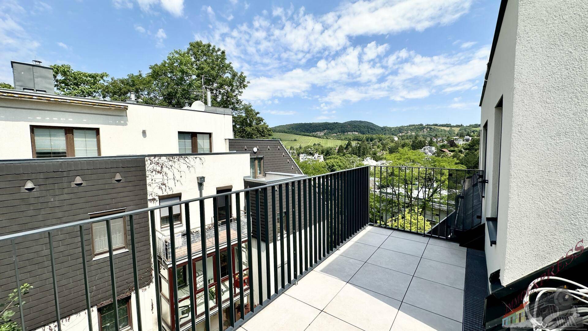 Dachterrasse mit Fliesenboden und weitem Blick über die grüne Landschaft und umliegende Häuser.