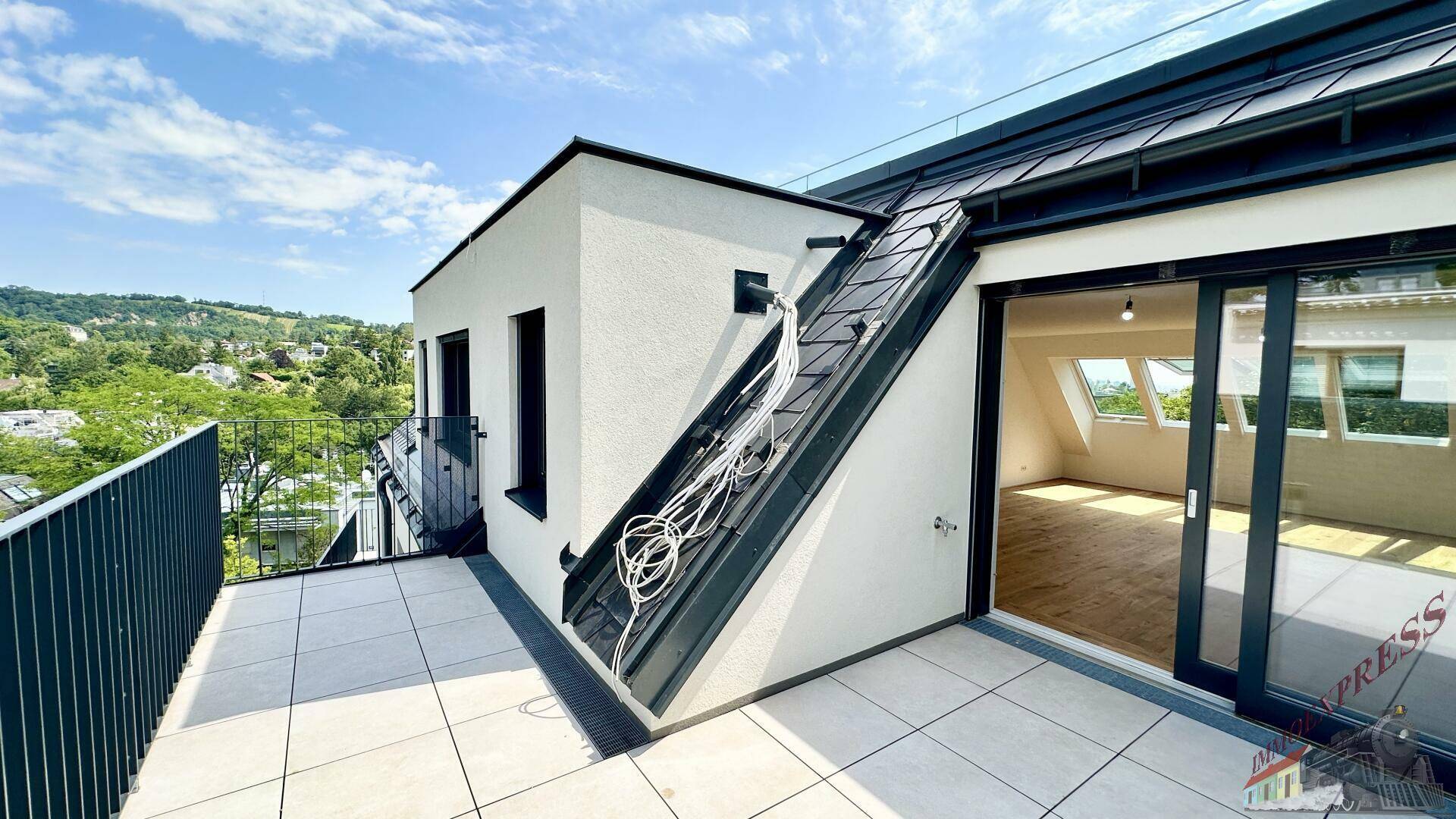 Dachterrasse mit Fliesenboden und Blick auf die grüne Umgebung und das Innere des Dachgeschosses.