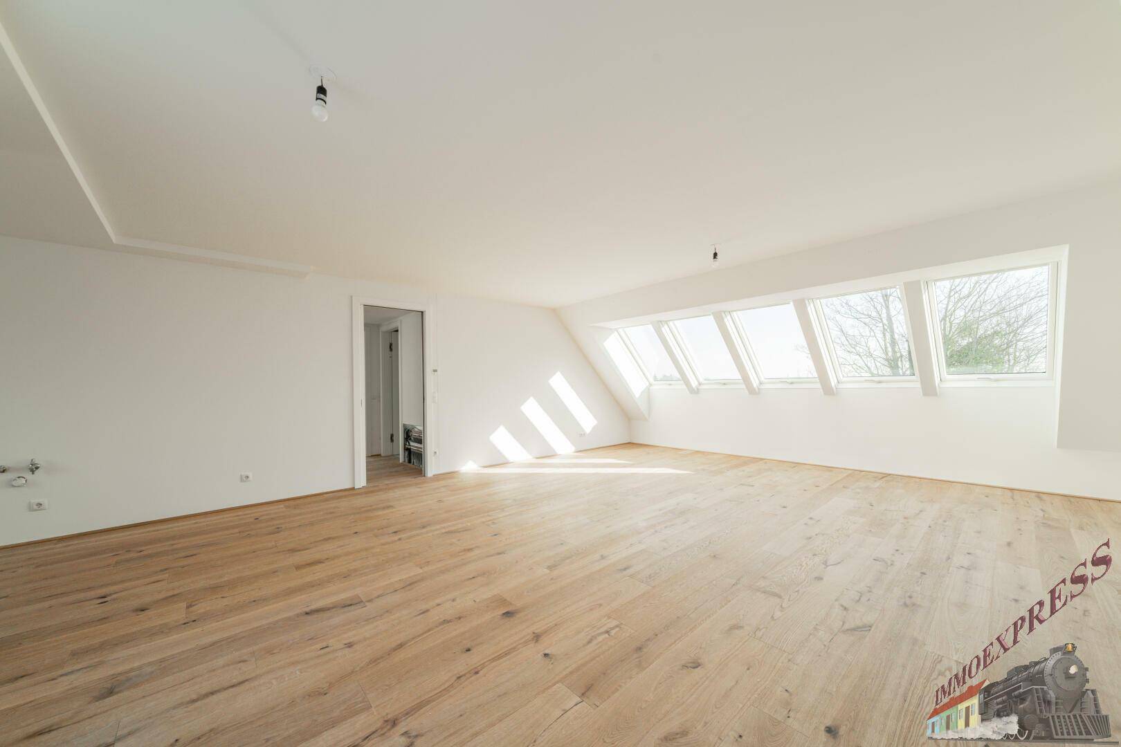 Helles Dachgeschosszimmer mit Holzboden und mehreren Dachfenstern, das viel Tageslicht hereinlässt.