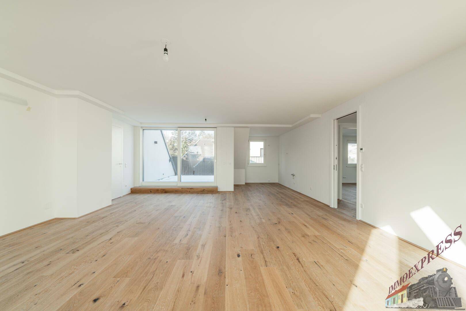Geräumiges Zimmer mit Holzboden, großer Schiebetür und Zugang zu weiteren Räumen.