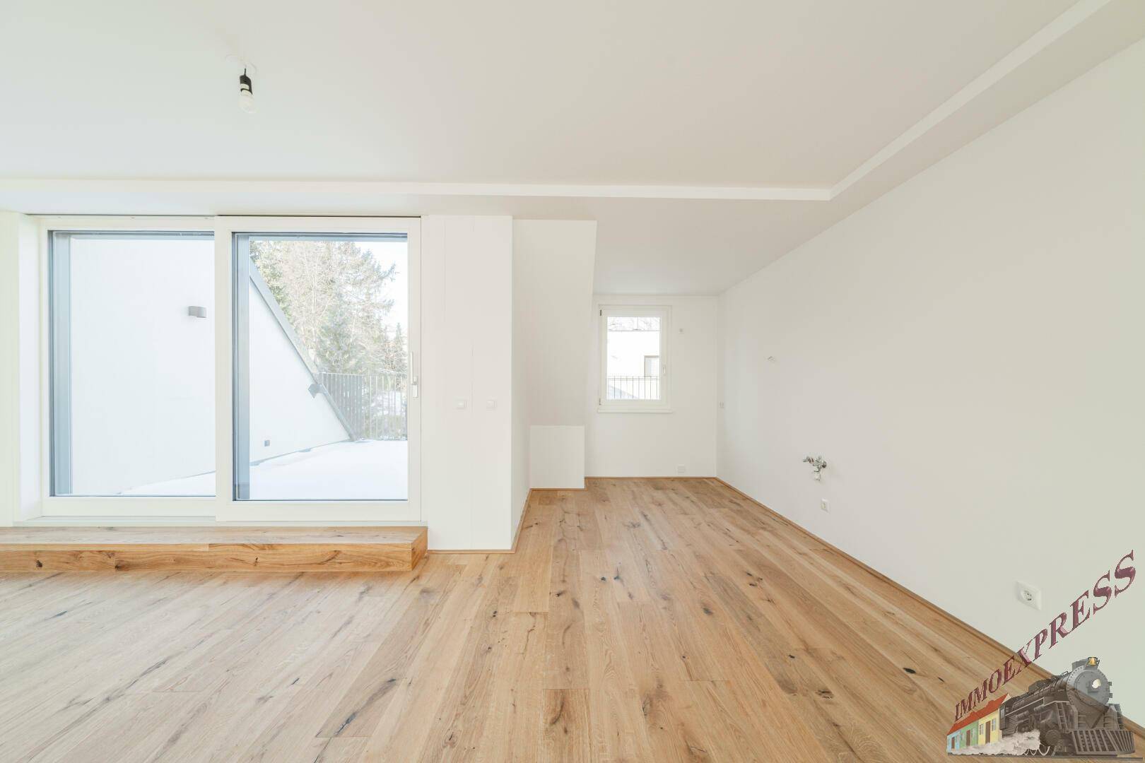 Helles Zimmer mit Holzboden und großer Schiebetür zu einem Außenbereich.