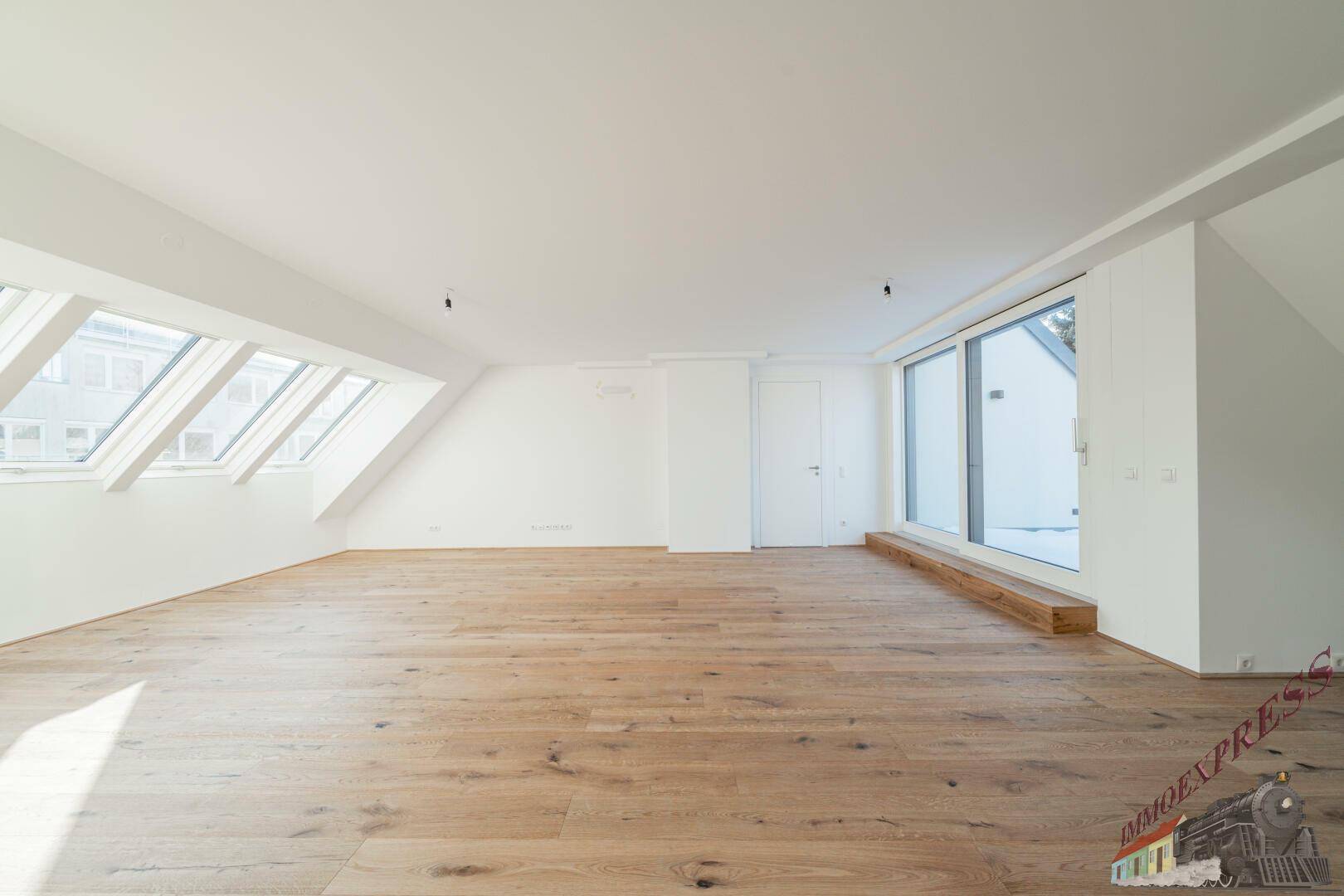 Geräumiges Zimmer im Dachgeschoss mit Holzboden, großen Fenstern und Zugang zu einem Außenbereich.