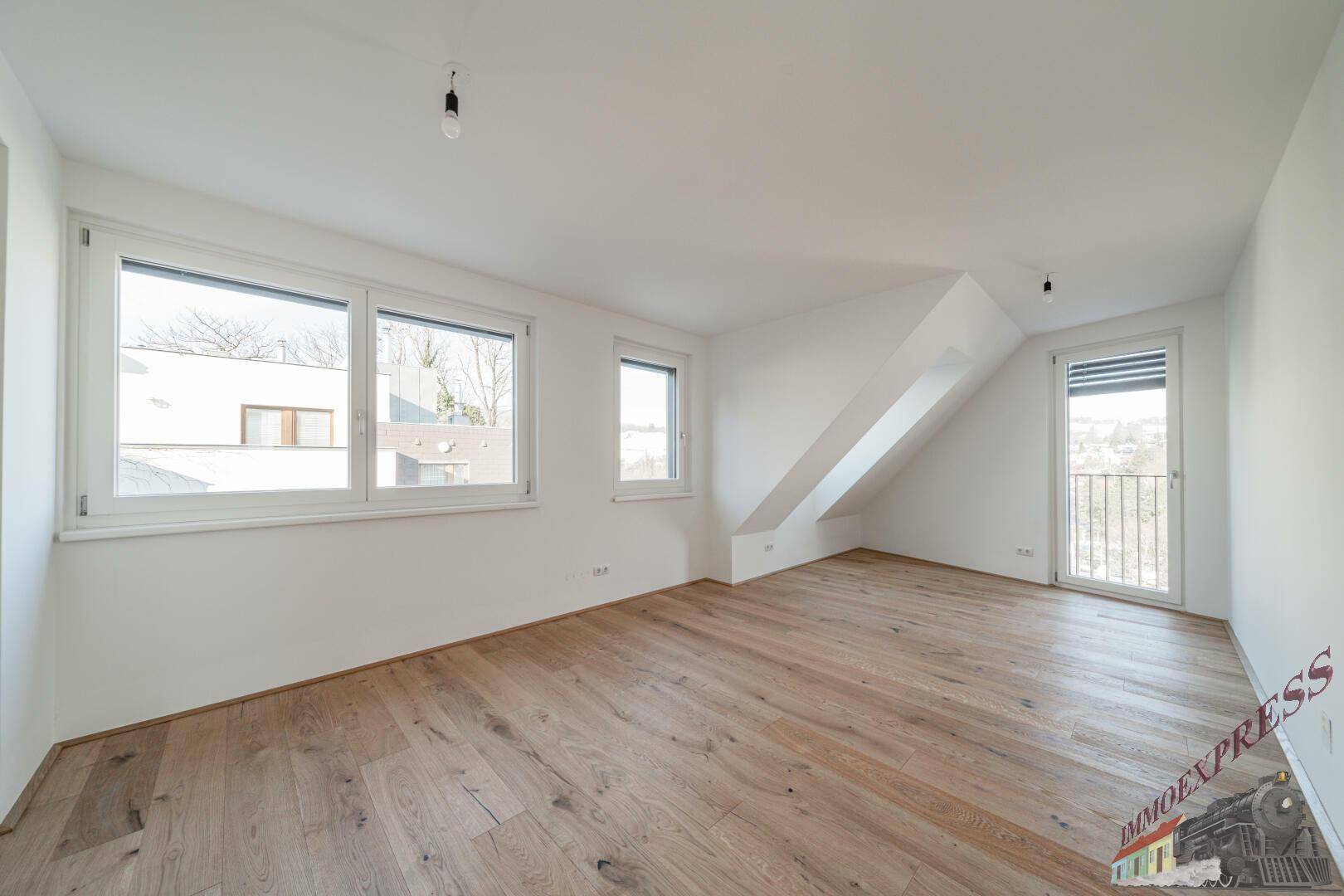 Helles Zimmer mit Holzboden, großen Fenstern und französischem Balkon.