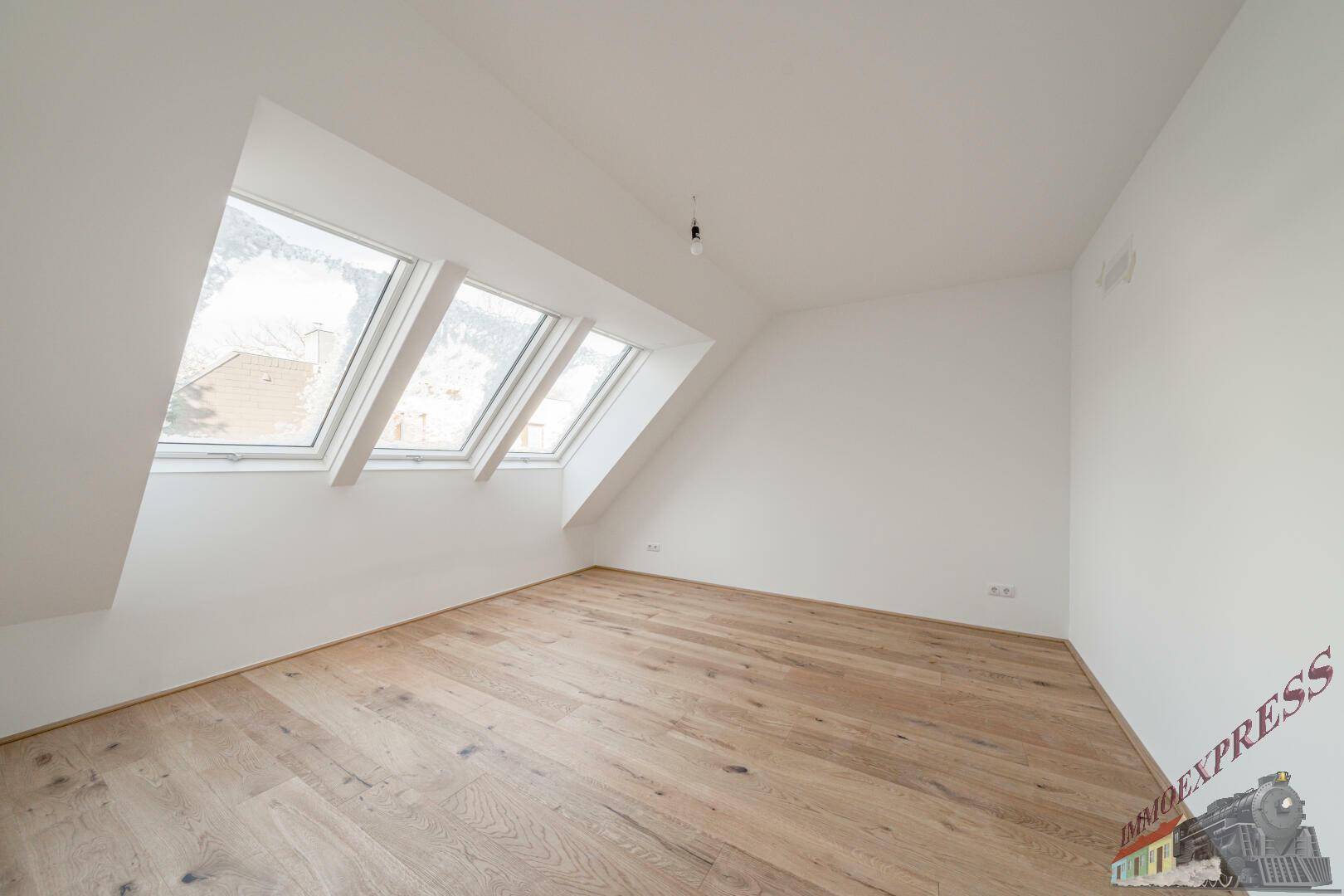 Helles Schlafzimmer im Dachgeschoss mit Holzboden und drei Dachfenstern.