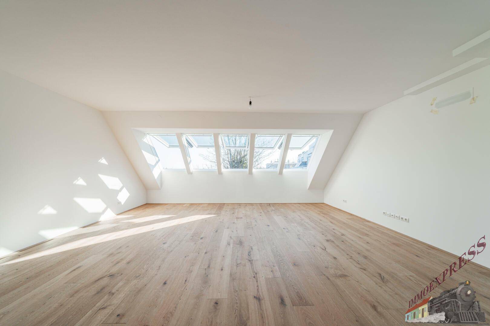 Helles Dachgeschosszimmer mit Holzboden und mehreren Dachfenstern, das viel Tageslicht hereinlässt.