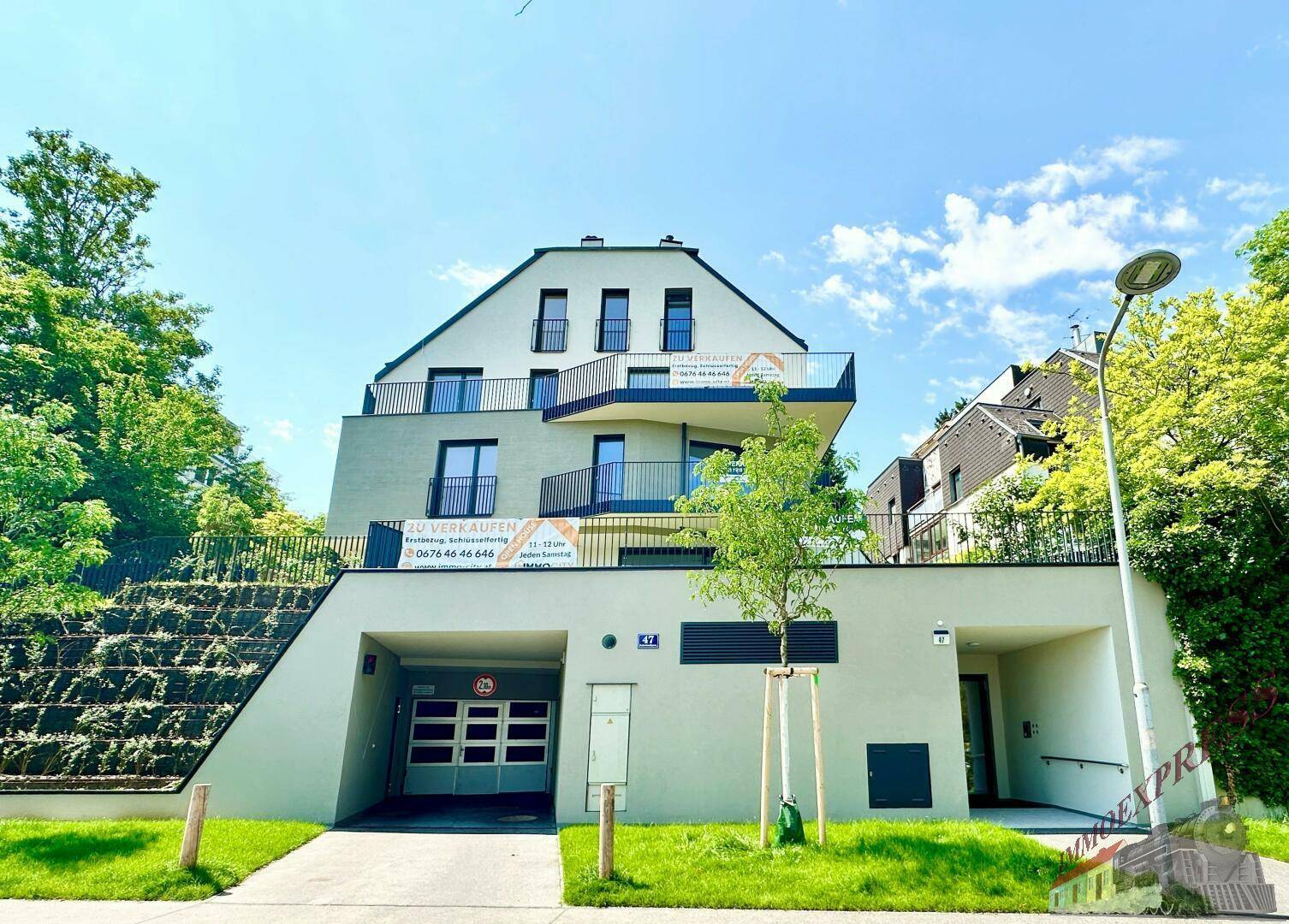 Moderne Wohnanlage mit mehreren Balkonen und Tiefgaragenzufahrt in grüner Umgebung.
