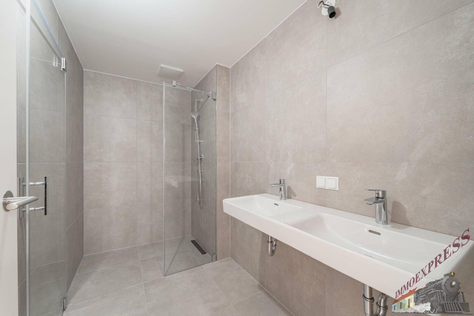 Modernes Badezimmer mit Doppelwaschbecken, großer begehbarer Dusche und hellen Fliesen.