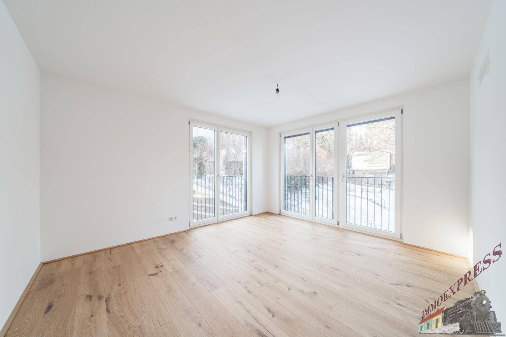 Lichtdurchflutetes Zimmer mit Parkettboden und Zugang zu einem französischen Balkon mit Blick ins Grüne.
