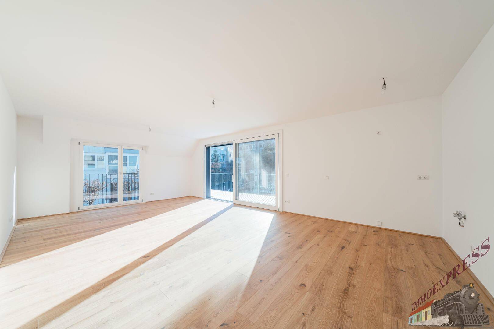 Helles Wohnzimmer mit Holzboden und großen Fenstern, die viel Sonnenlicht hereinlassen.