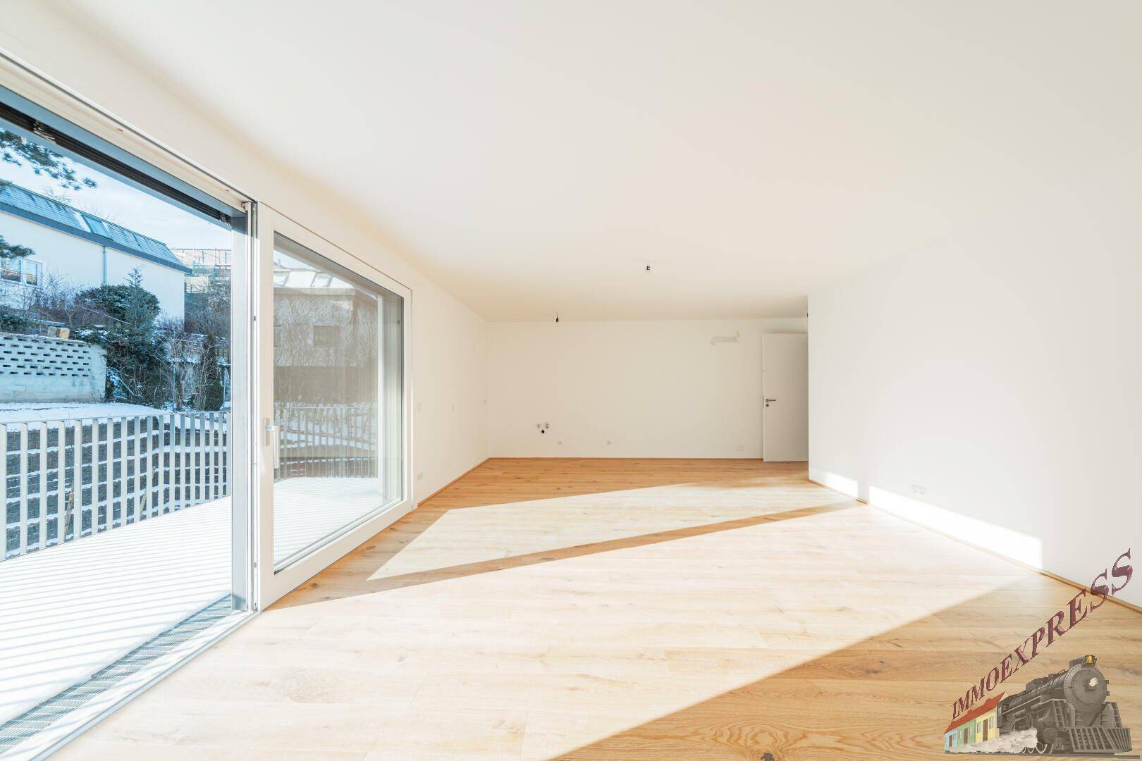 Helles Wohnzimmer mit Holzboden und großen Fenstern, die viel Sonnenlicht hereinlassen.