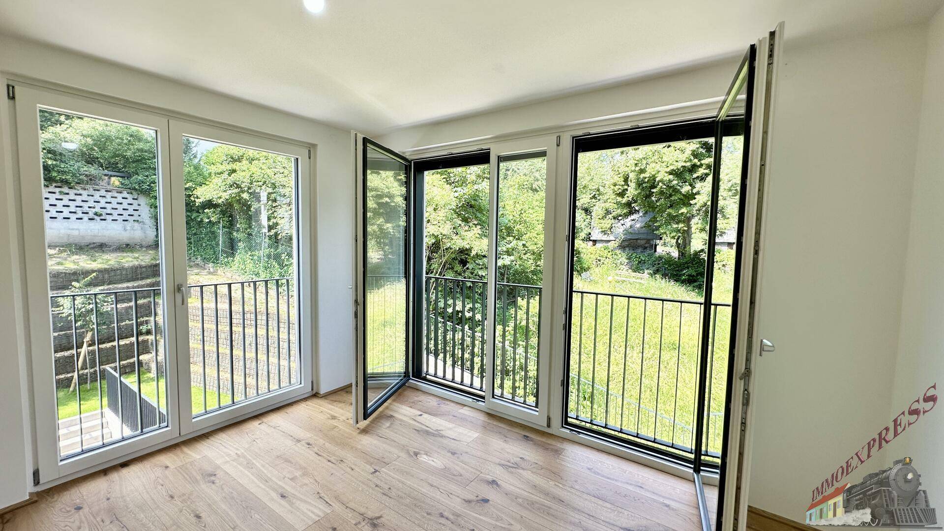 Lichtdurchflutetes Zimmer mit Parkettboden und Zugang zu einem französischen Balkon mit Blick ins Grüne.
