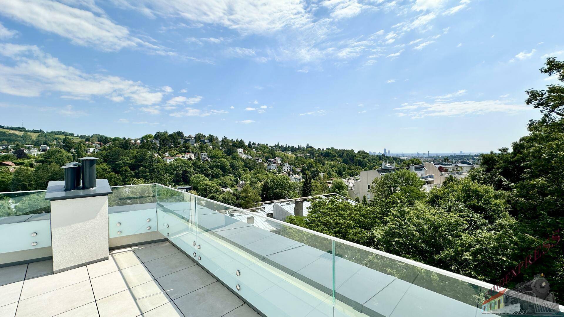 Sonniger Terrassenbereich mit weitem Blick über die Baumwipfel und die Stadt in der Ferne.