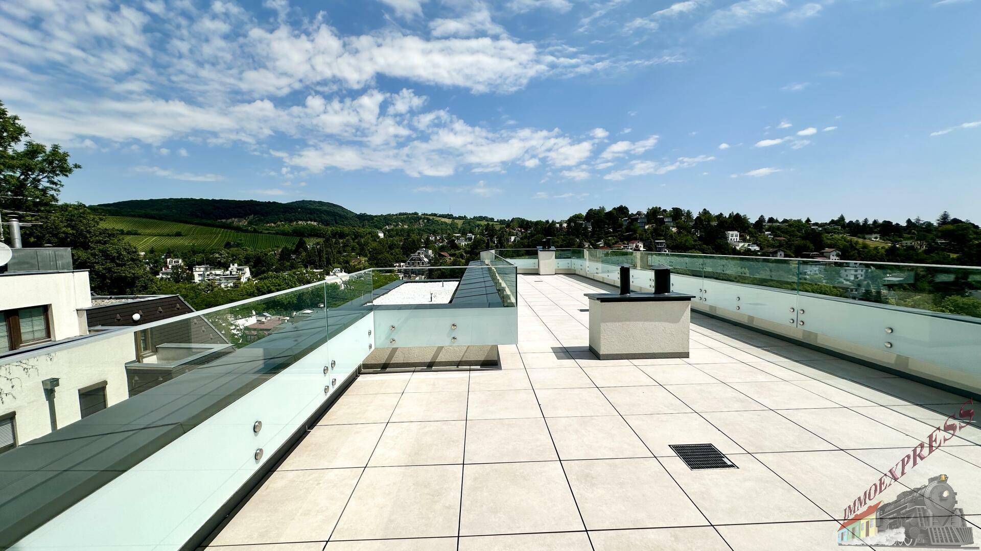 Weitläufige Dachterrasse mit Fliesenboden und Glasgeländer, bietet viel Platz im Freien.