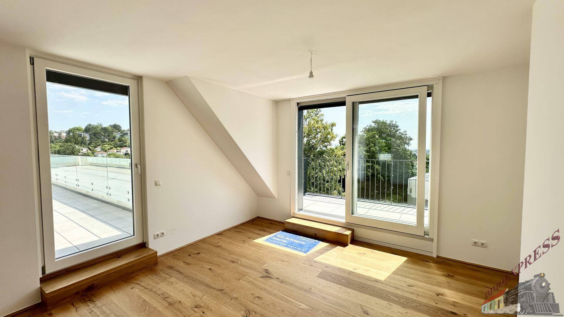 Helles Zimmer mit Holzboden und großen Fenstern, die auf eine sonnige Terrasse führen.
