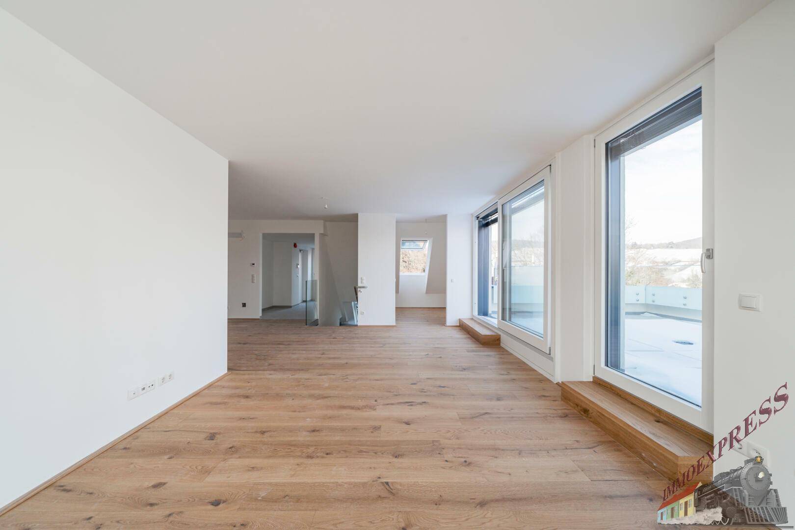 Geräumiger, heller Wohnbereich mit Holzboden und großen Fenstern, die viel Licht hereinlassen.