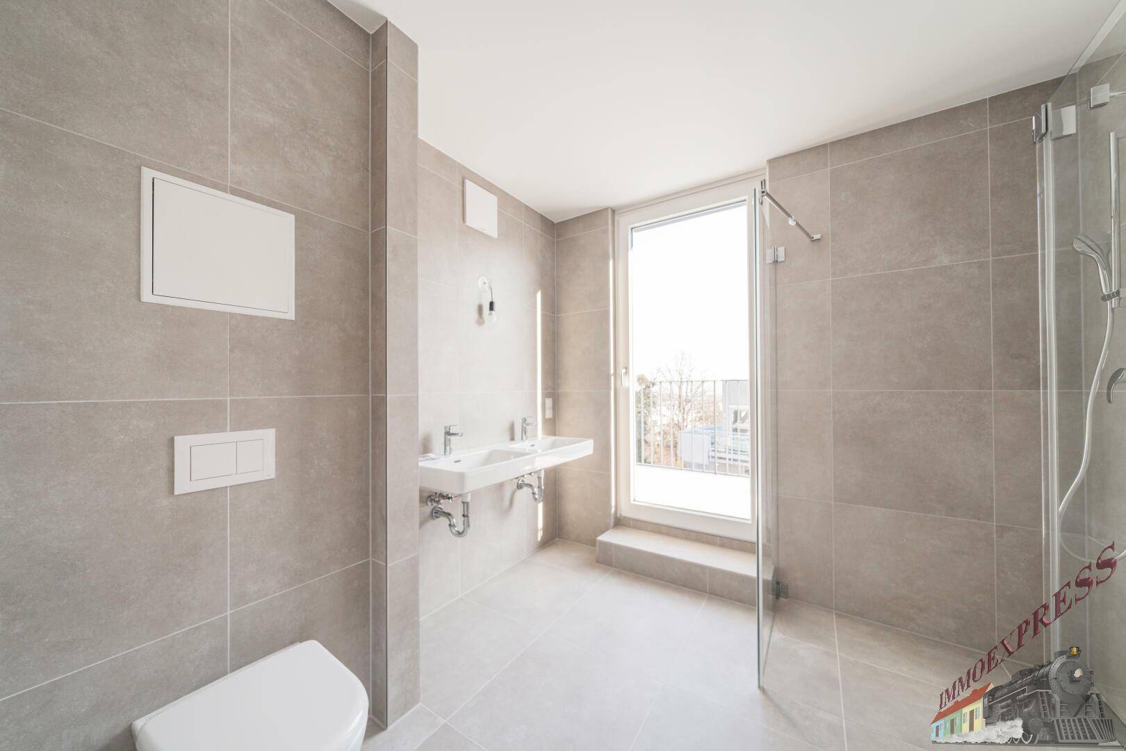 Zeitgemäßes Badezimmer mit Doppelwaschbecken, wandmontierter Toilette und großer Dusche.