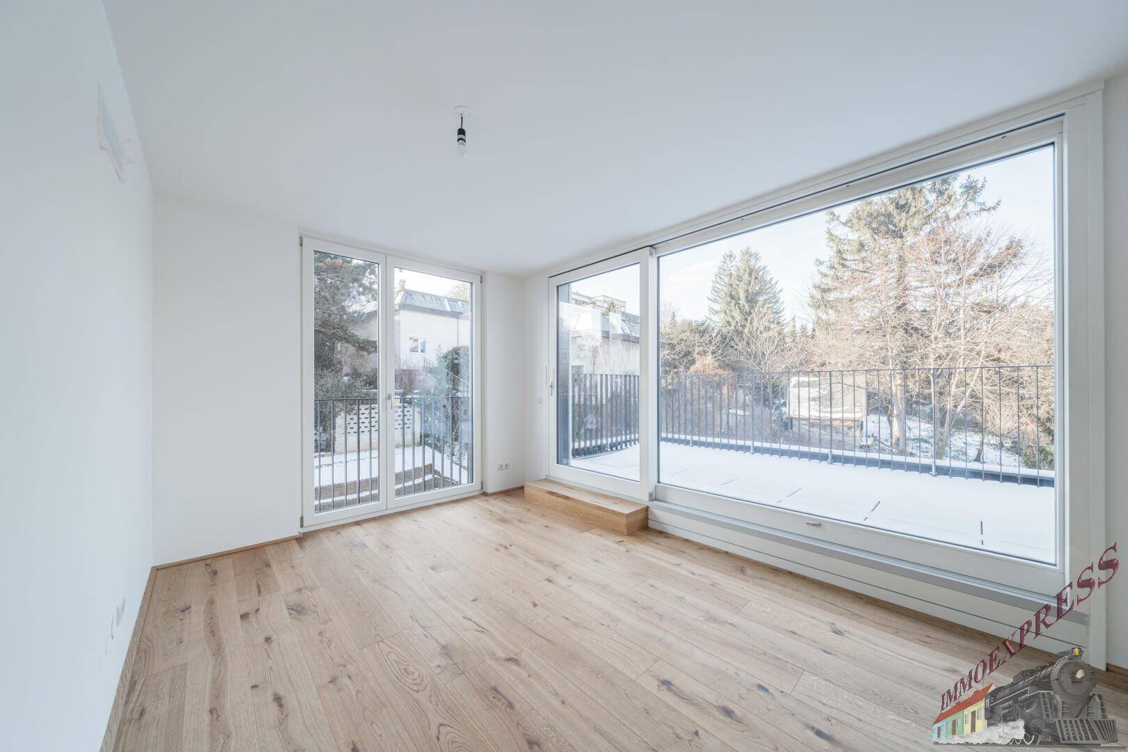 Lichtdurchflutetes Zimmer mit Holzboden und breiten Fenstern, die Zugang zur Terrasse ermöglichen.