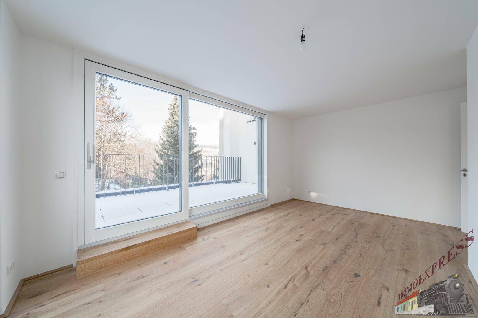 Geräumiges Zimmer mit Holzboden und großen Schiebetüren, die auf eine Terrasse führen.