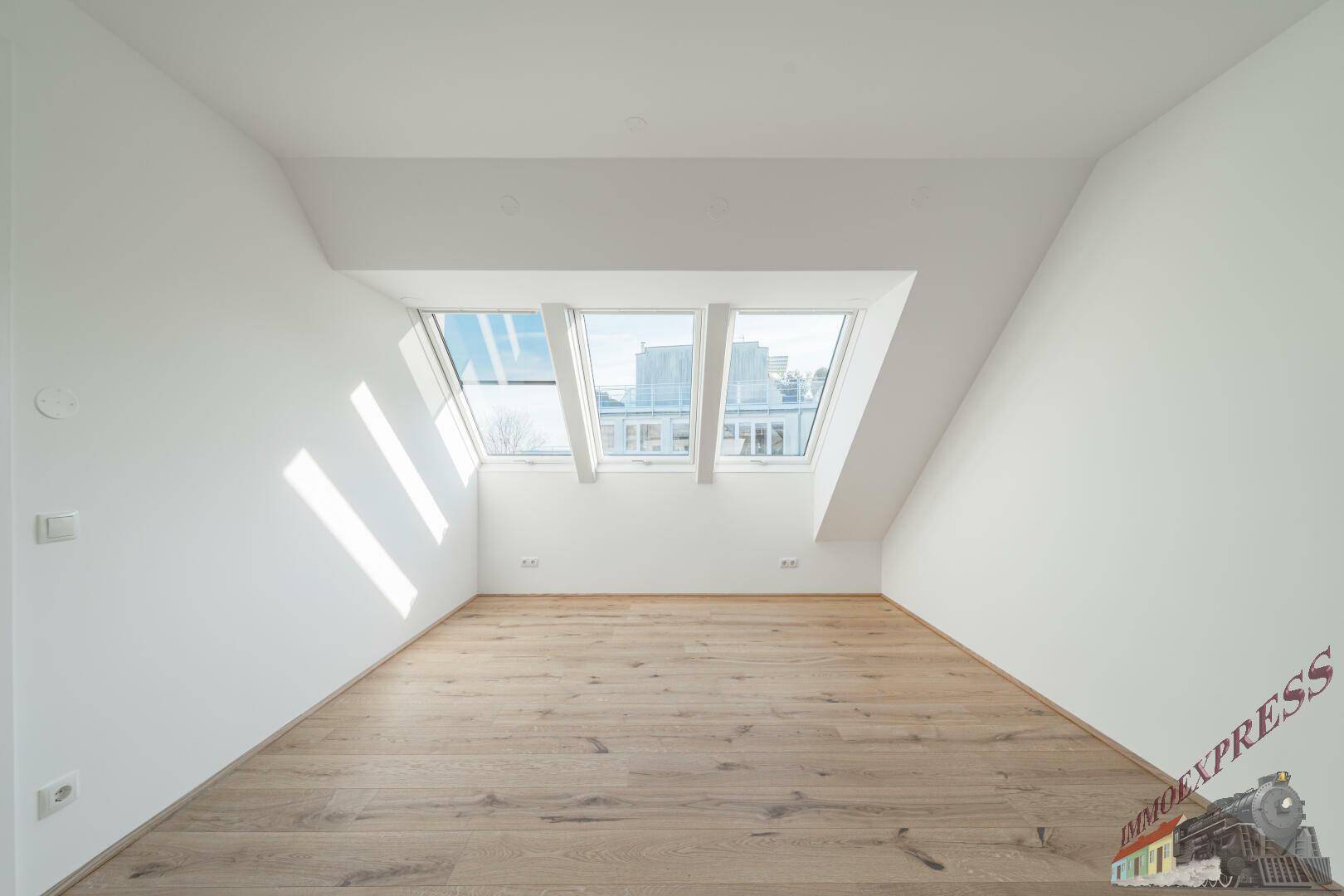 Helles Zimmer im Dachgeschoss mit Holzboden und drei Dachfenstern, die viel Licht spenden.