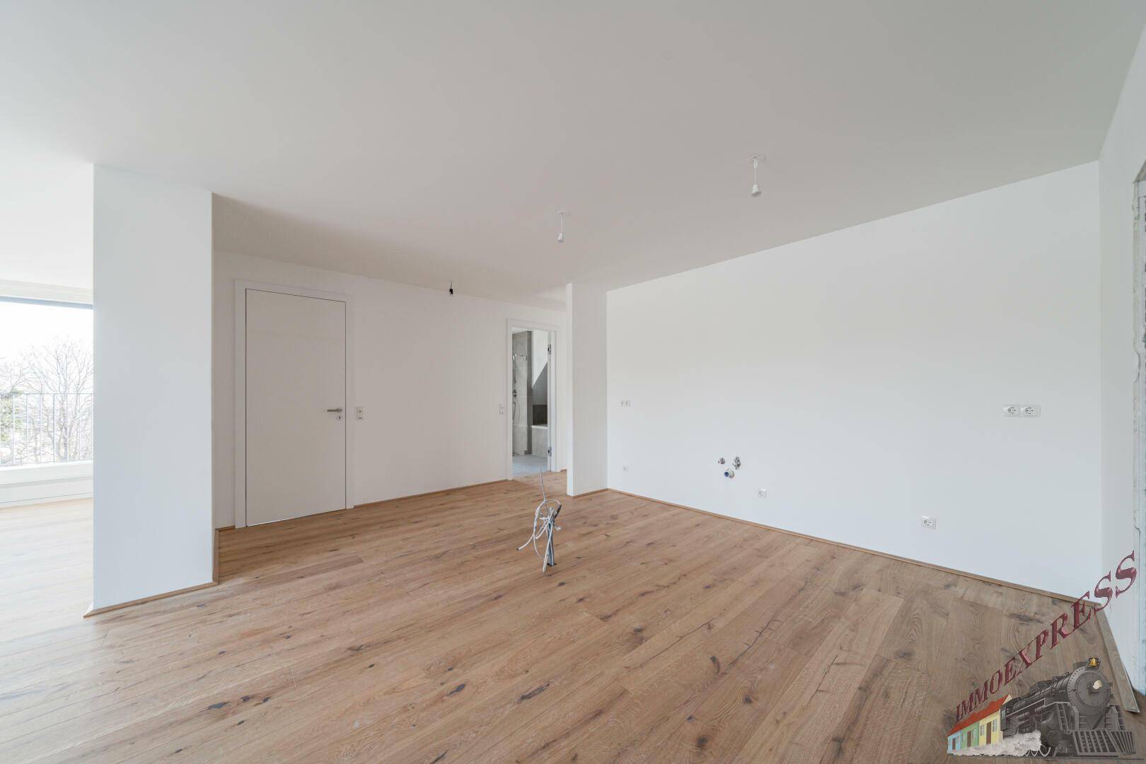 Geräumiger, heller Raum mit Holzboden und weißen Wänden, ideal für ein offenes Wohnkonzept.