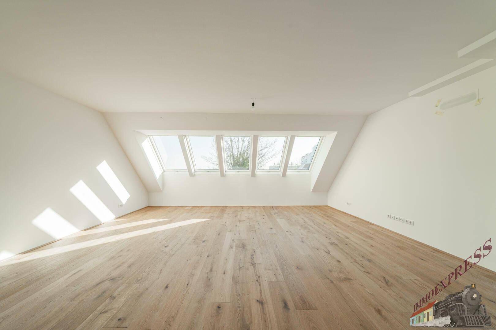 Helles, leeres Zimmer im Dachgeschoss mit Holzboden und großen Dachfenstern.