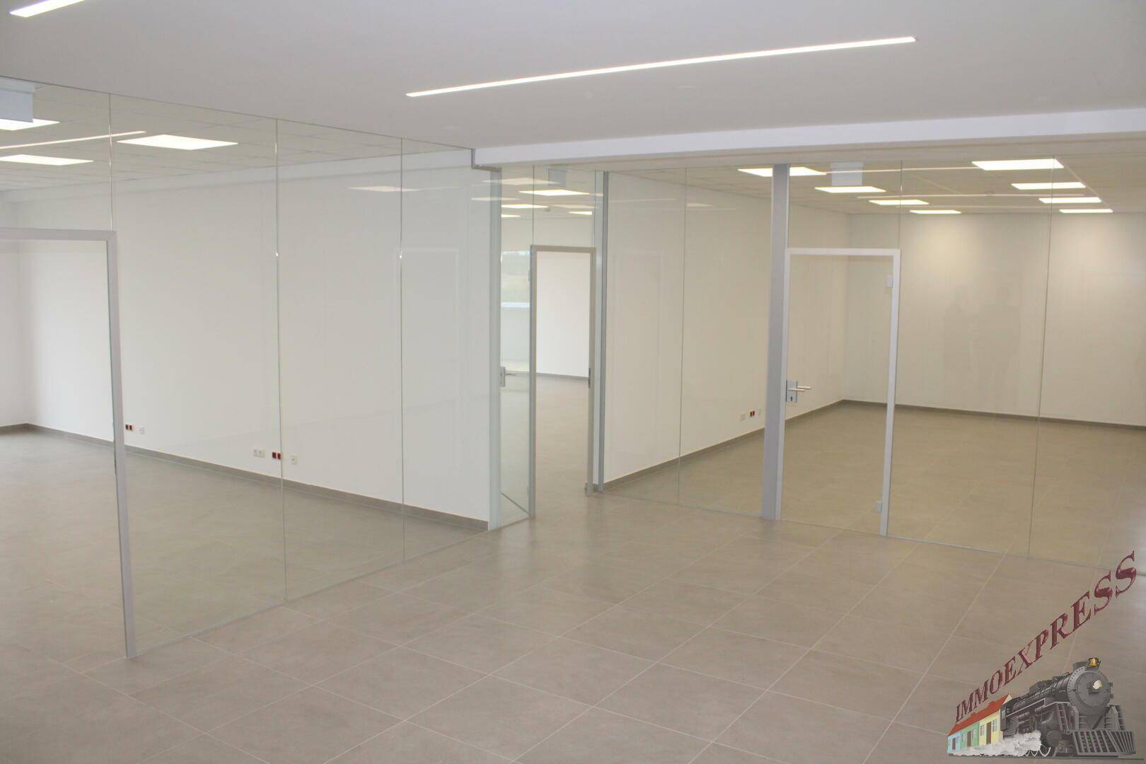 Moderner Bürobereich mit Glaswänden, Fliesenboden und heller Deckenbeleuchtung, ideal für offene Arbeitskonzepte.