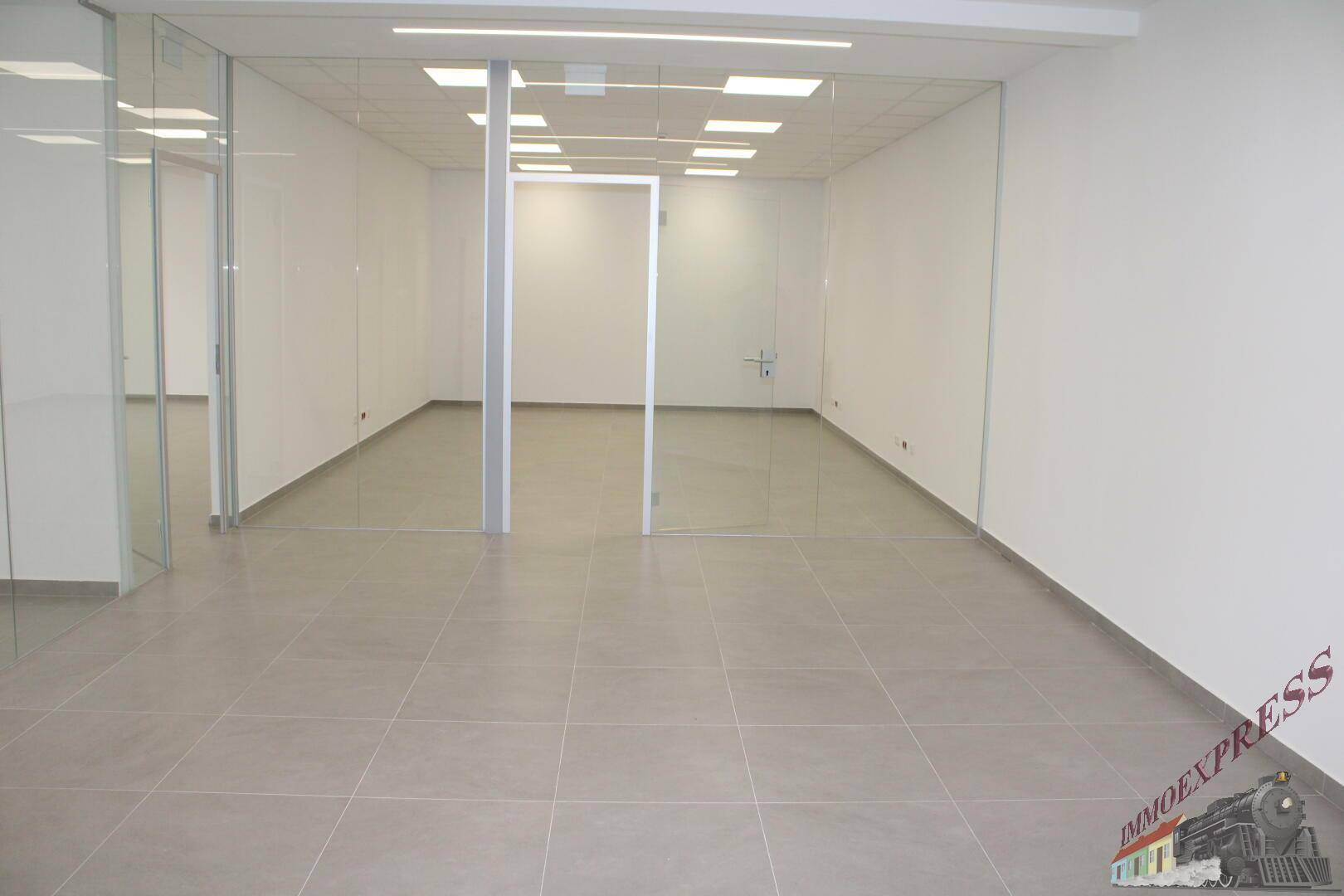 Langer, heller Bürobereich mit Glasabtrennungen und modernem Fliesenboden, schafft eine offene Arbeitsatmosphäre.