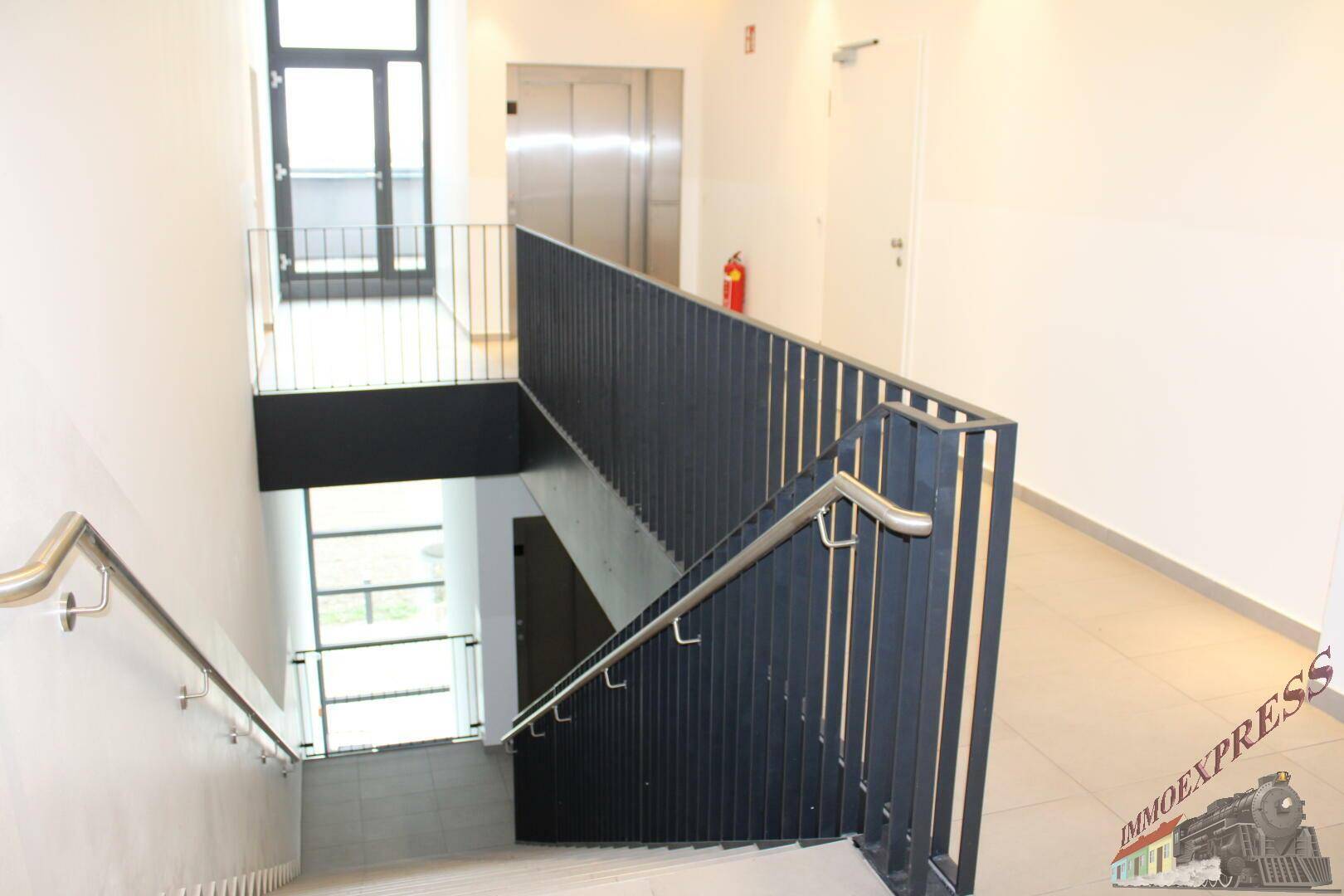 Modernes Treppenhaus mit schwarzem Metallgeländer und hellem Fliesenboden, verbindet die verschiedenen Ebenen.
