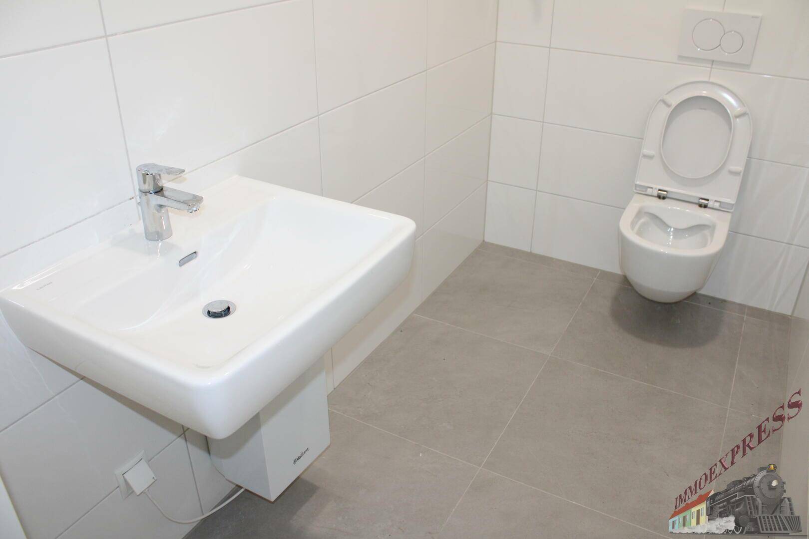Saubere und moderne Gästetoilette mit Wand-WC und Waschbecken, komplett gefliest in Weiß und Grau.
