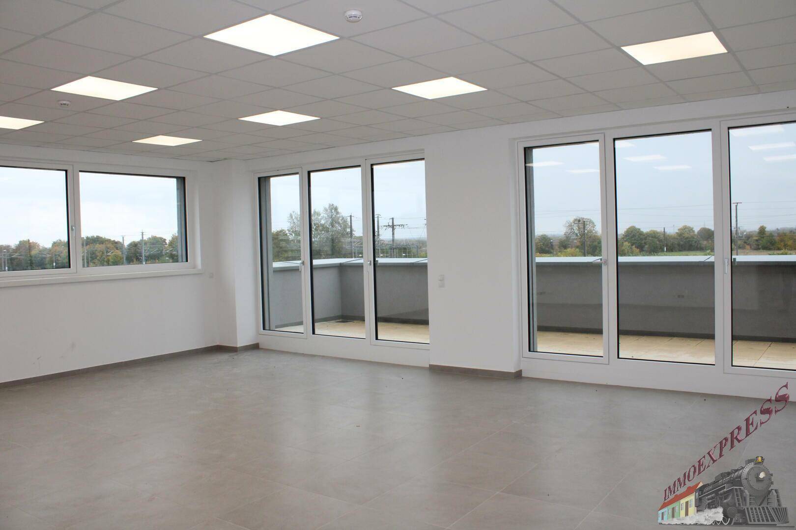 Heller Büroraum mit großen Fenstern und Zugang zu einem Balkon, bietet viel Tageslicht und eine weite Aussicht.
