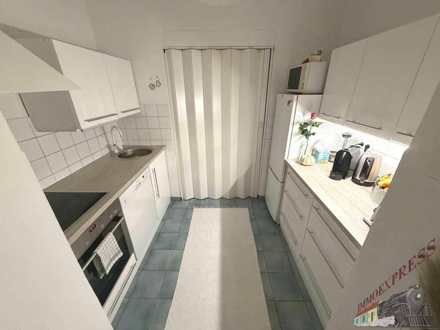 Funktionale Küche mit weißen Schränken, blauen Fliesen und integrierten Geräten.