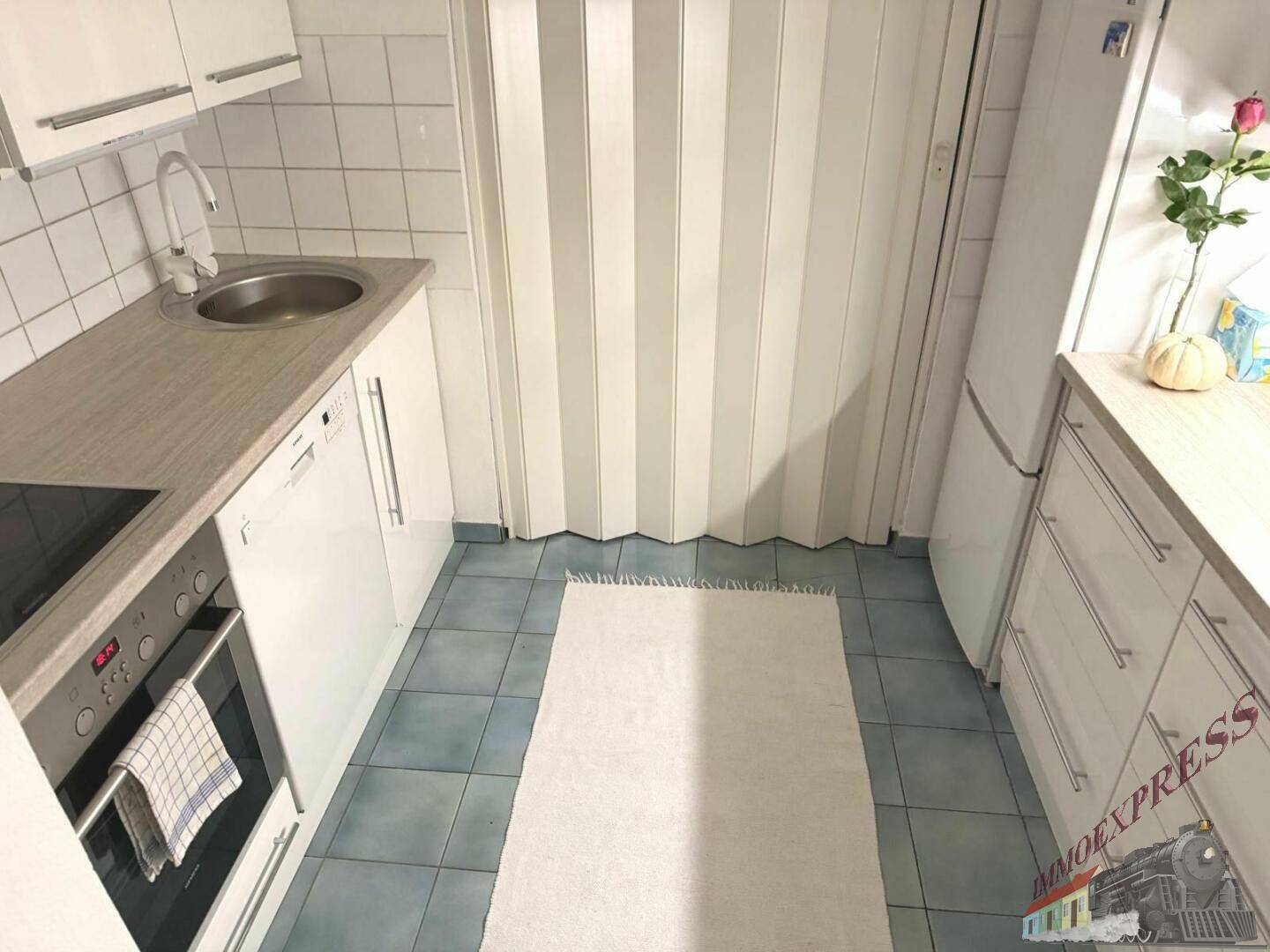 Kompakte Küche mit weißen Einbauschränken, blauen Bodenfliesen und praktischer Ausstattung.