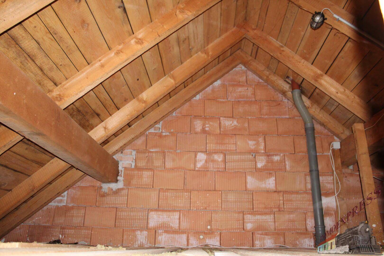 Unausgebauter Dachboden mit sichtbaren Holzbalken und Ziegelwänden.