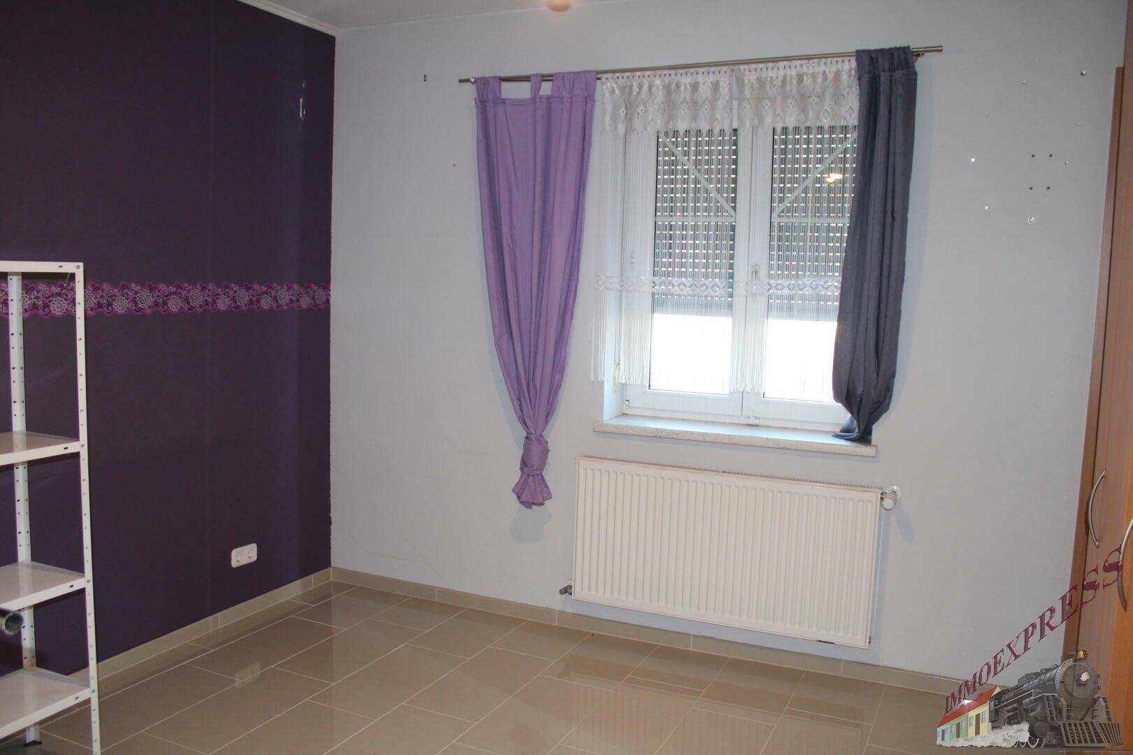 Schlafzimmer mit lila Akzentwand, Fenster und Heizkörper.