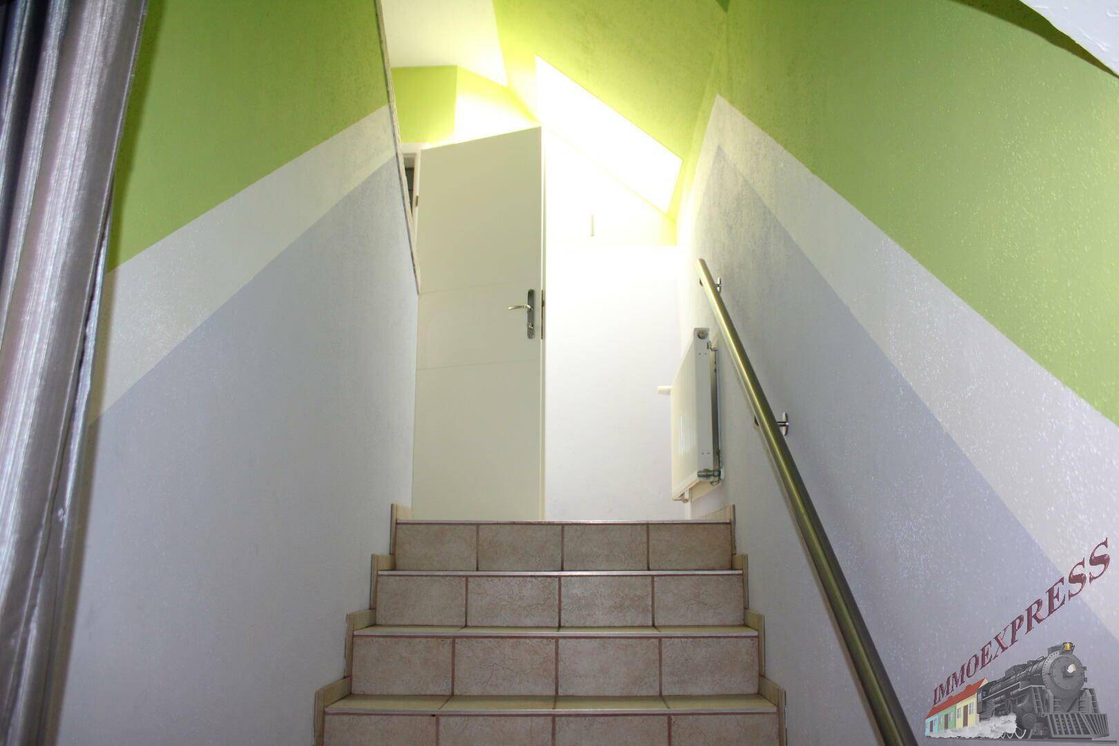 Treppenhaus mit gefliesten Stufen, Handlauf und farbigen Wänden.