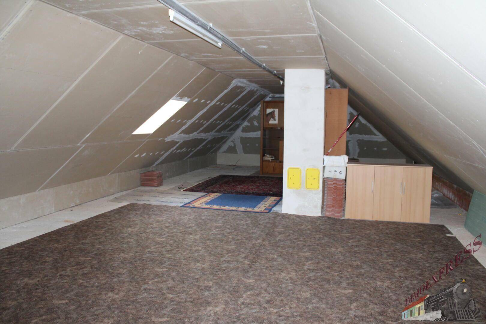 Ausbaufähiger Dachboden mit schrägen Wänden und Teppichboden.
