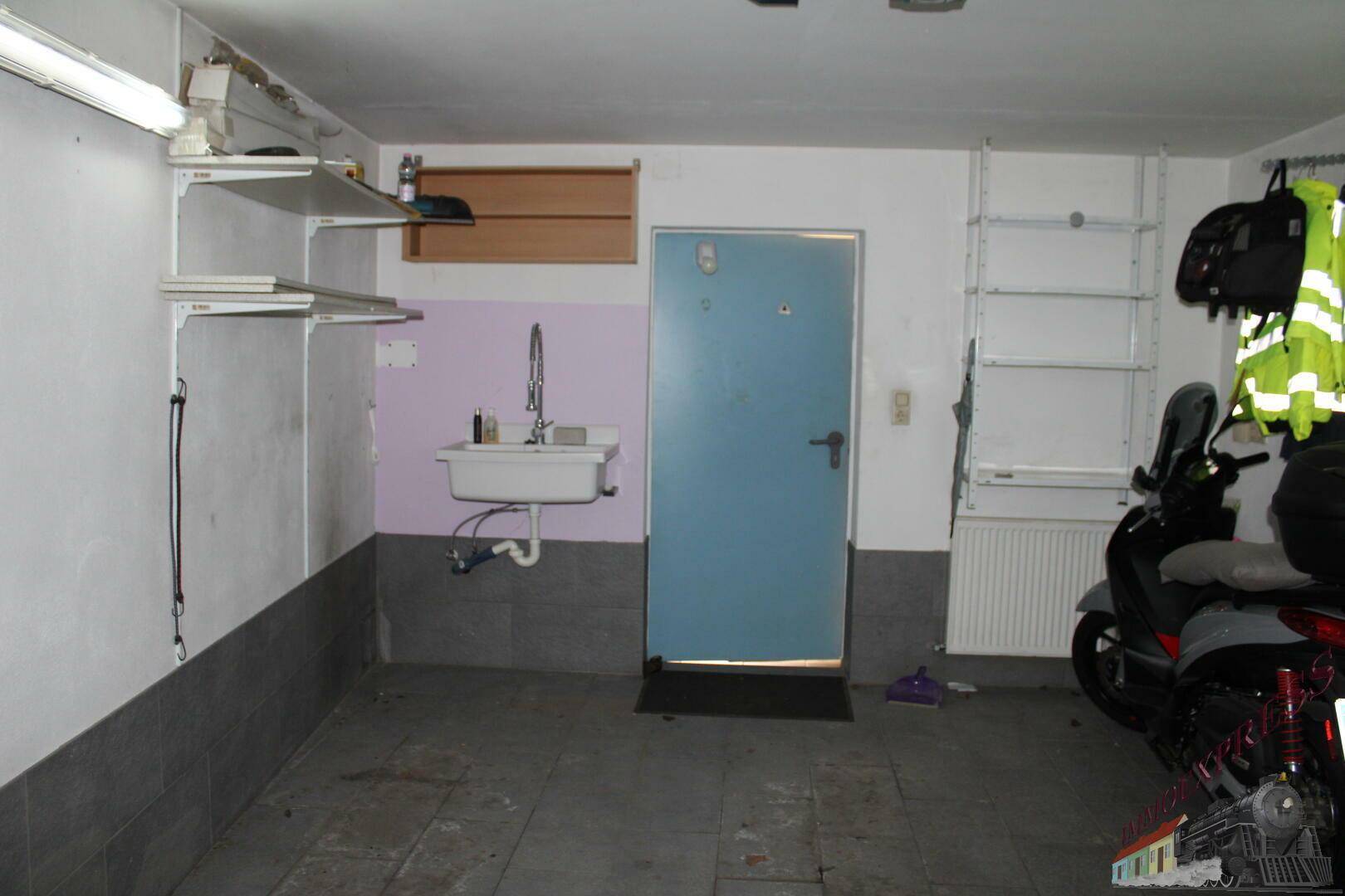 Garage mit Waschbecken, Regalen und Zugangstür.