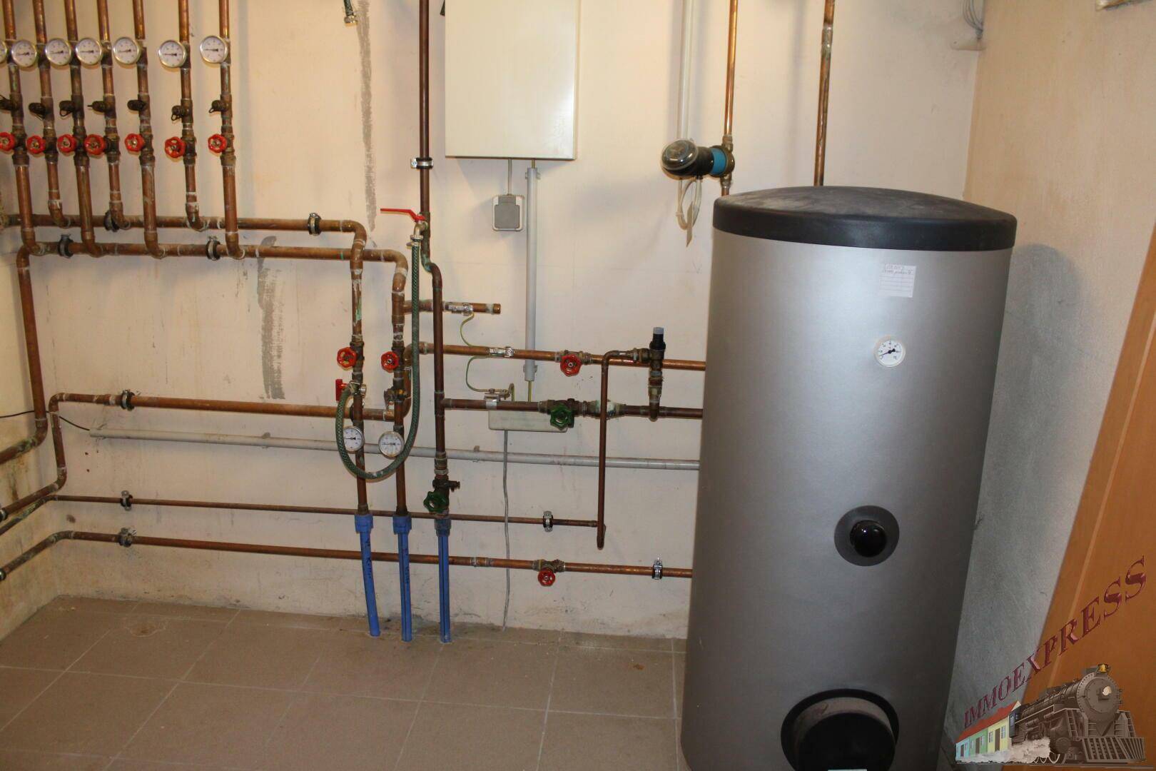 Heizungsraum mit Warmwasserspeicher und komplexer Rohrinstallation.