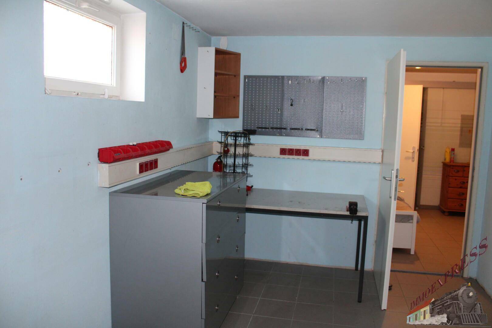 Werkstattraum im Keller mit Arbeitsplatte, Regalen und Fenster.