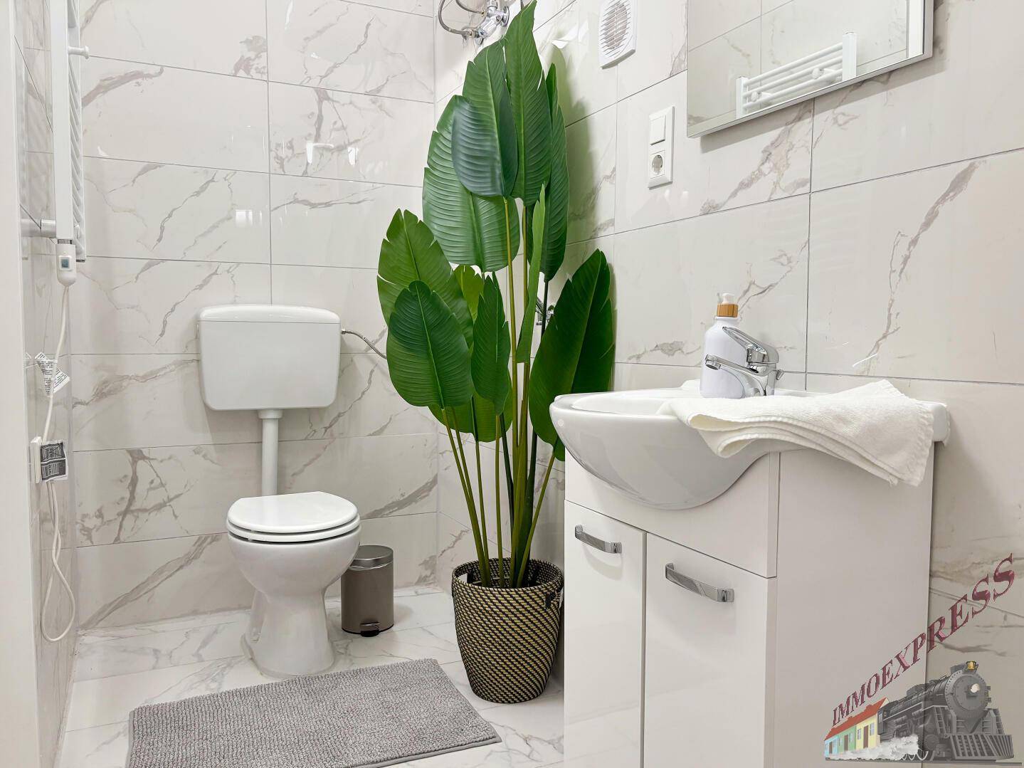 Helles Badezimmer mit modernem WC, Waschbecken und einer dekorativen Pflanze.