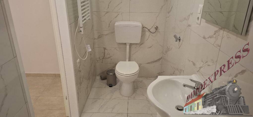 Funktionales Badezimmer mit WC, Waschbecken und Handtuchheizkörper, komplett gefliest in Marmoroptik.