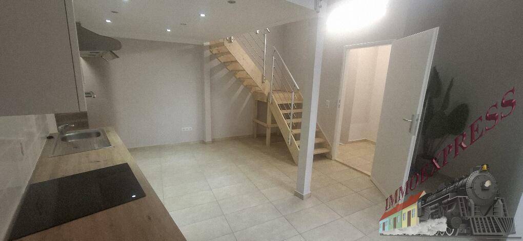 Geräumiger, leerer Raum mit Fliesenboden, Holztreppe und einer Tür, die zu einem weiteren Bereich führt.