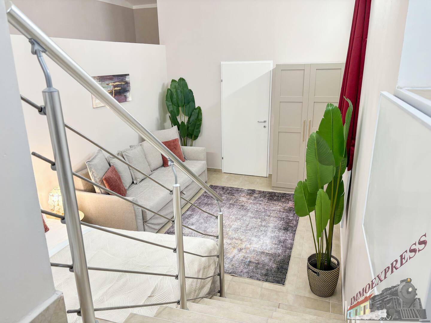 Blick von der Treppe auf einen gemütlichen Wohnbereich mit Sofa, Teppich und dekorativer Pflanze.