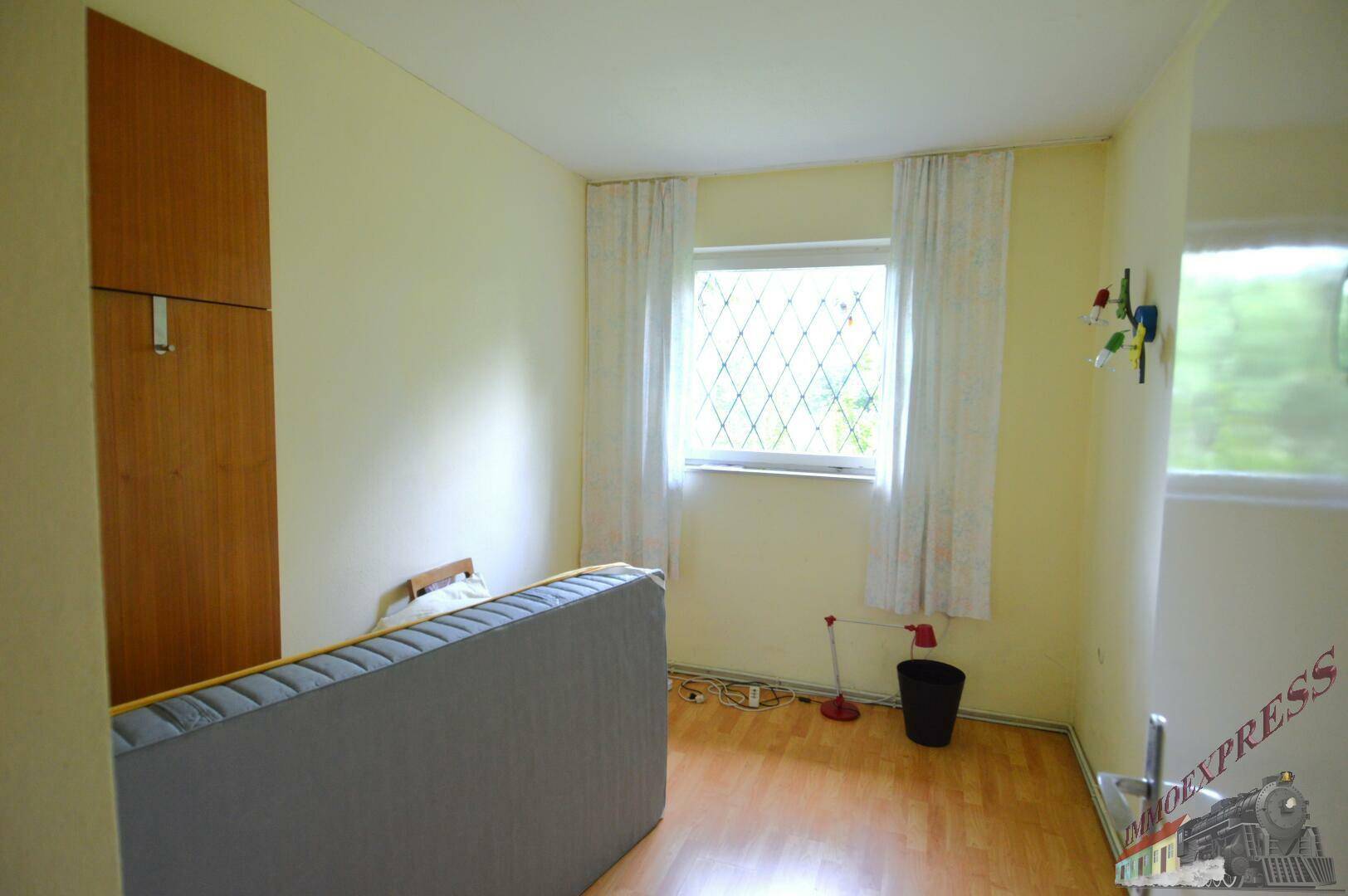 Helles Schlafzimmer mit Laminatboden, einem Kleiderschrank und einem Fenster mit Blick ins Grüne.
