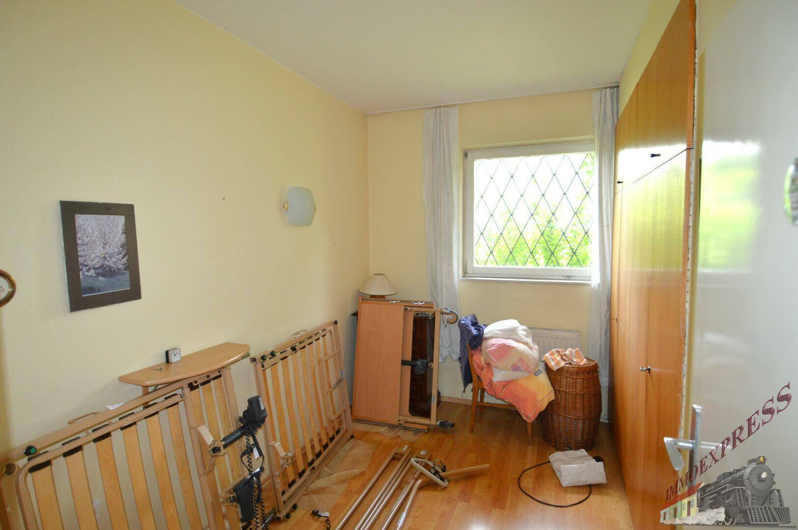 Schlafzimmer mit Laminatboden, einem Kleiderschrank und einem Fenster mit Blick ins Grüne.