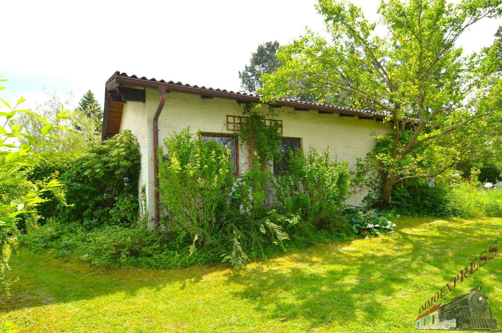 Seitenansicht des Hauses mit bewachsenen Wänden und einem Satteldach in ländlicher Umgebung.
