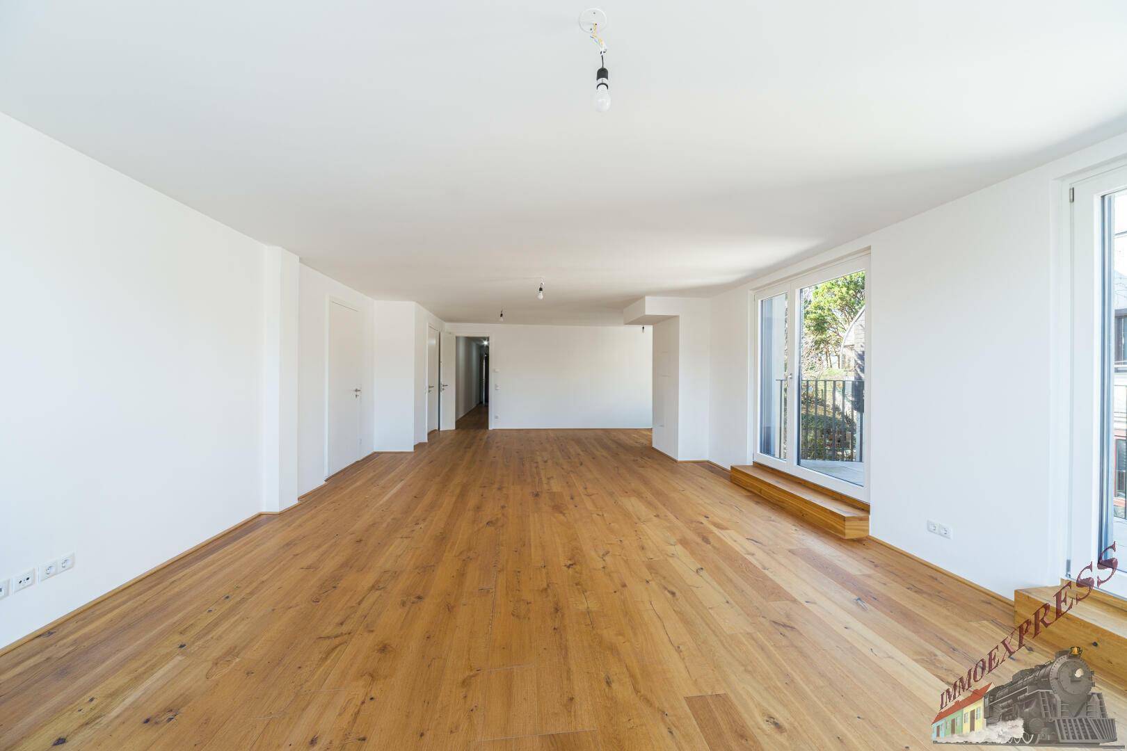 Geräumiger Wohnbereich mit Holzboden und großen Fenstern, ideal für viel Licht.