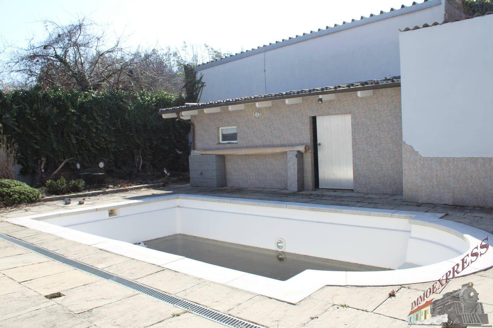 Außenbereich mit leerem Pool, gepflasterter Fläche und Nebengebäude.